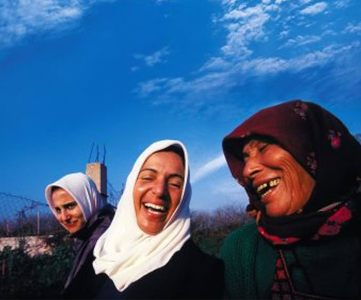 映画『ガーダ　パレスチナの詩』の場面。青空の下、ガーダを中心に３人のパレスチナ人が笑っている。