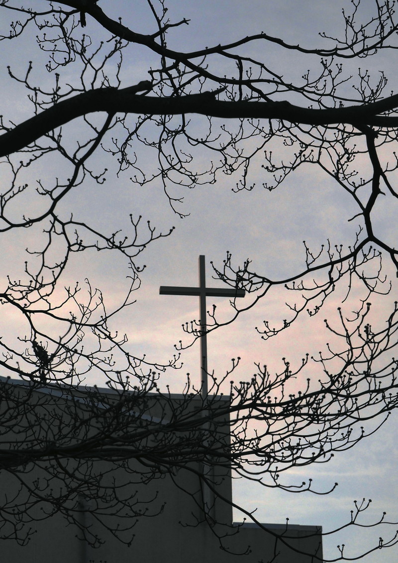 夕暮れの空に立つ十字架と前景のハナミズキの枯れ枝