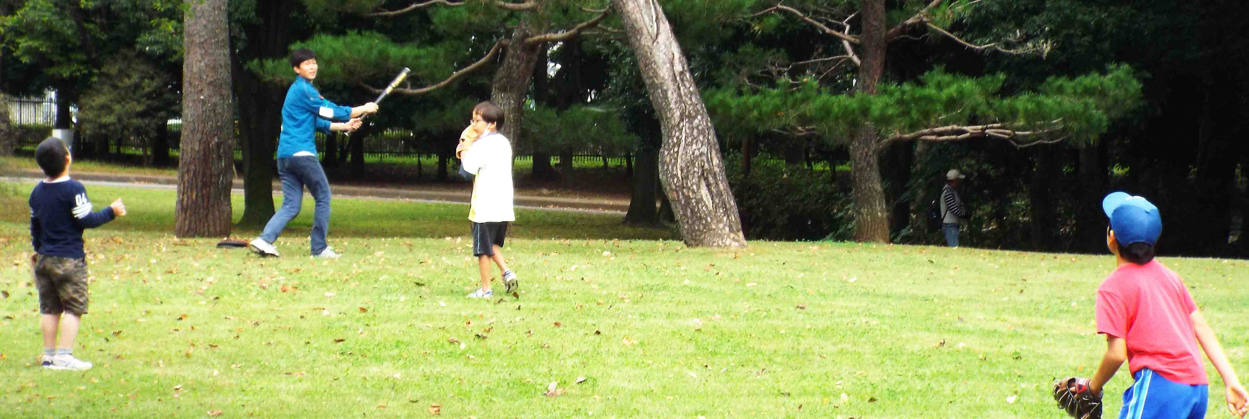 木々に囲まれた国立女性教育会館の緑の芝生の上で、子どもたちが野球を楽しんでいる写真