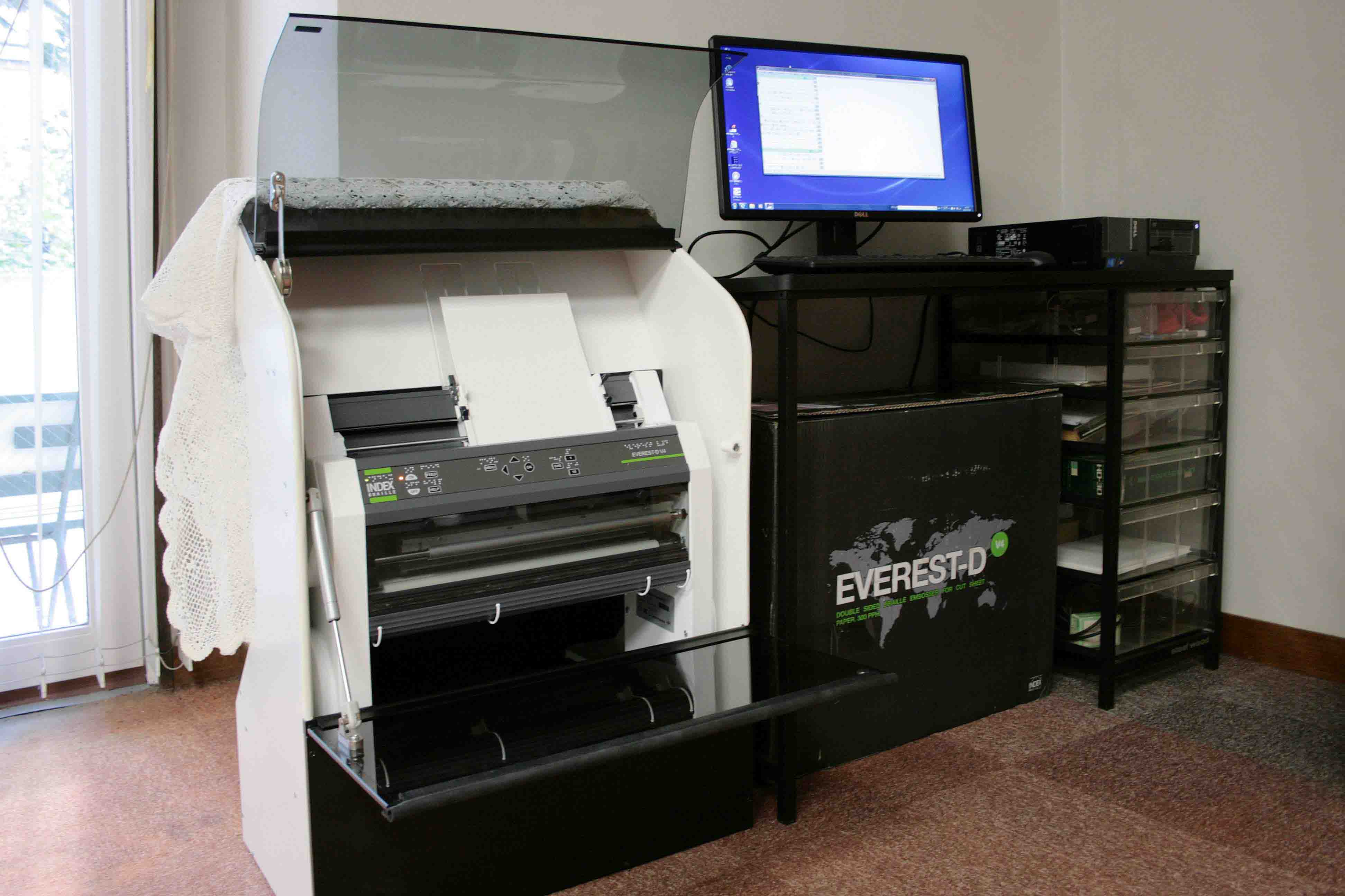 2015年11月に導入した、当会の新規点字プリンターの写真。横の作業台には点訳や点字プリンターをコントロールするパソコンとディスプレイが置かれています。